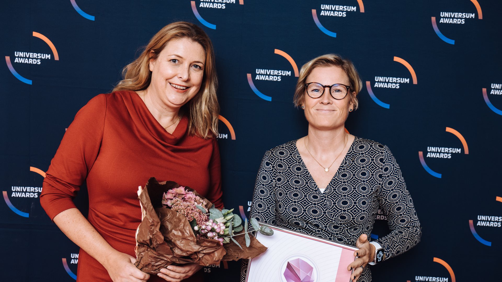 Två leende kvinnor med diplom och blombukett