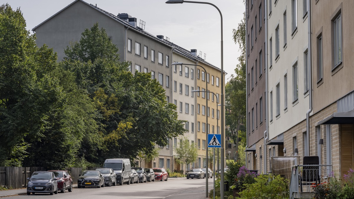 Gata i Stockholm med flerbostadshus, parkerade bilar och trottoar.