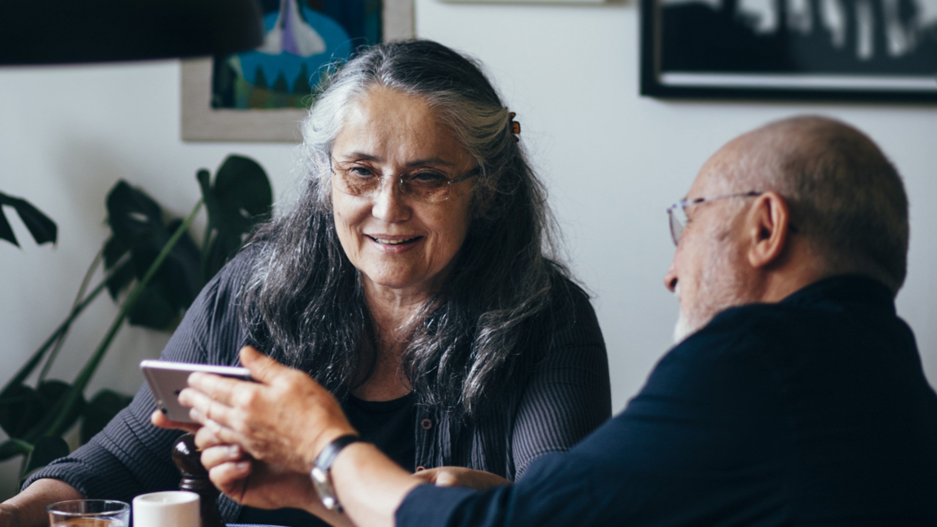Senior man showing mobile phone to woman at dining table