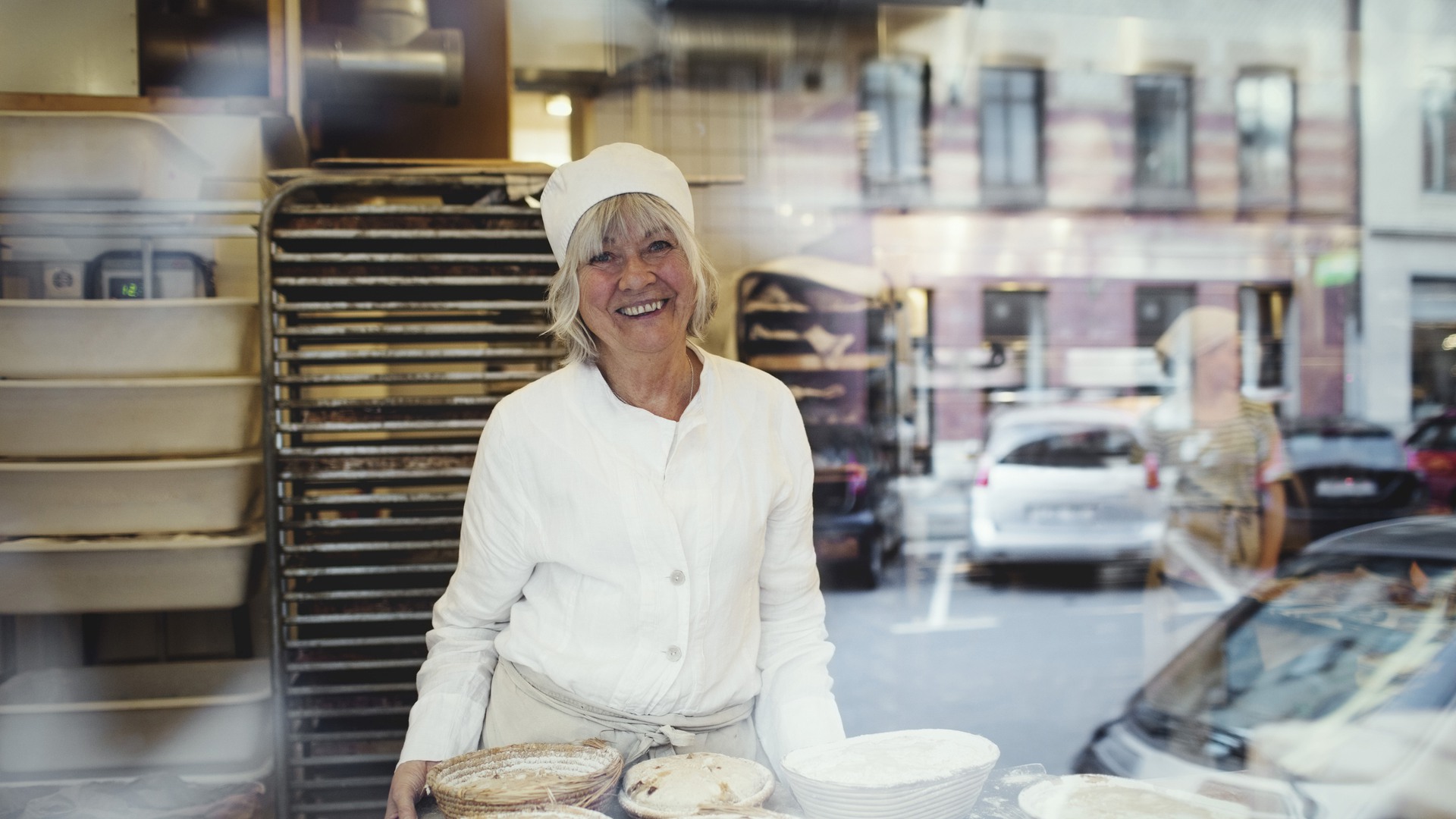 Portrait of senior smiling baker at bakery seen from glass window