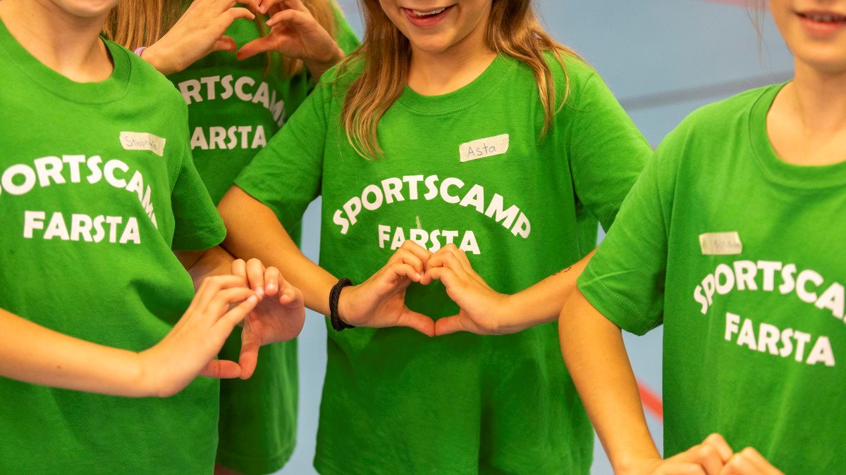Ett gäng tjejer i 10-årsåldern med gröna t-shirts med texten "Sportscamp Farsta" gör handhjärtan