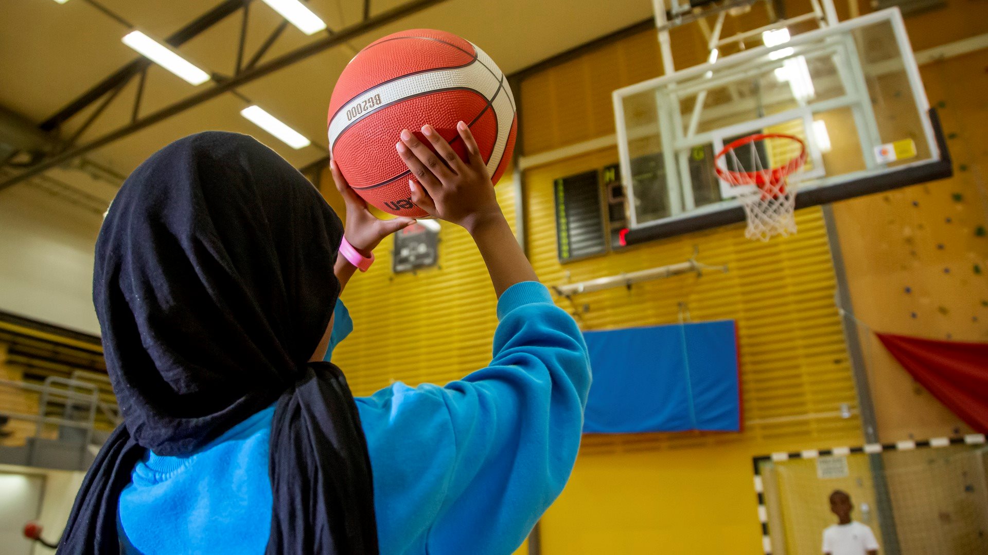 Flicka siktar med basketboll på basketkorg