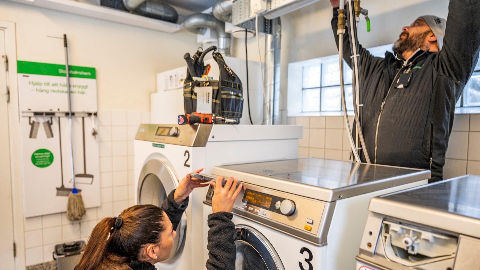 Två tekniker undersöker en tvättmaskin