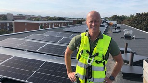 Man i varselväst på hustak med solceller