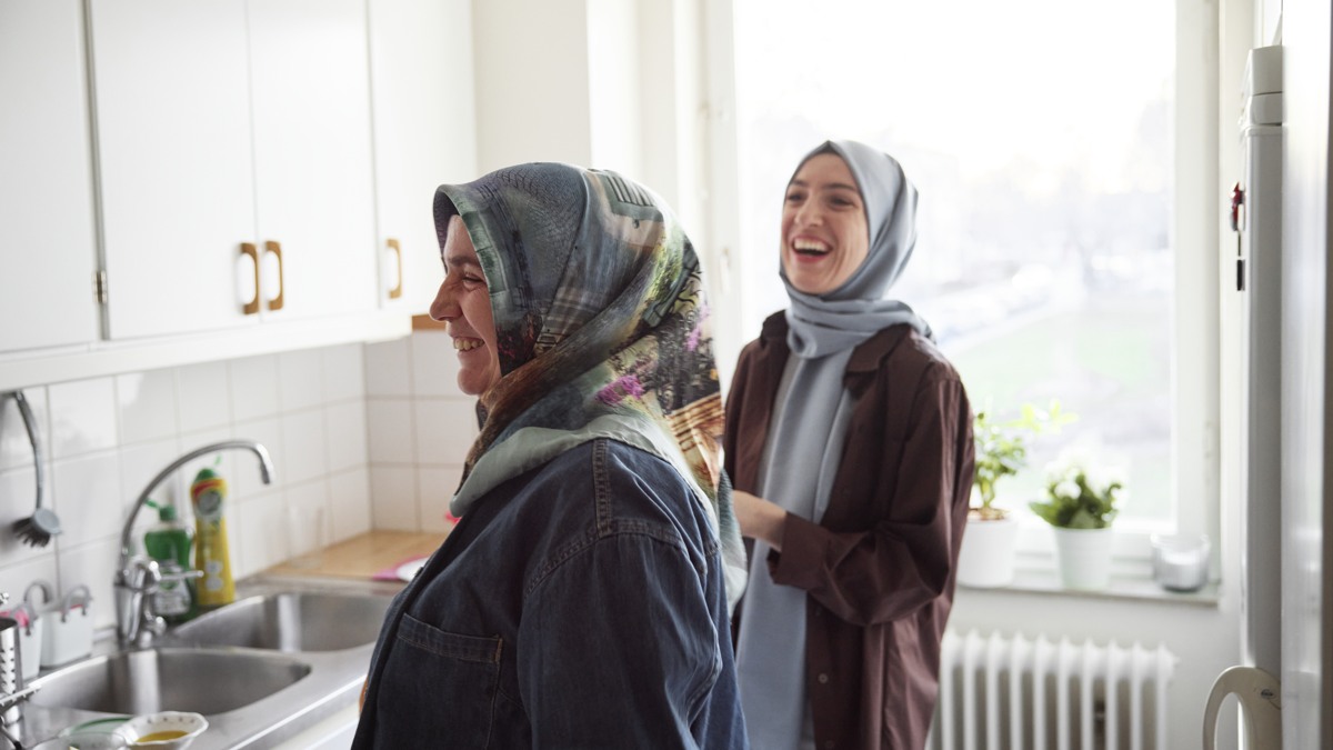 Mor och vuxen dotter i slöja skrattar i kök
