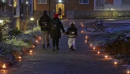 Marschaller längs mörk gångväg, familj med förskolebarn i lucialinne