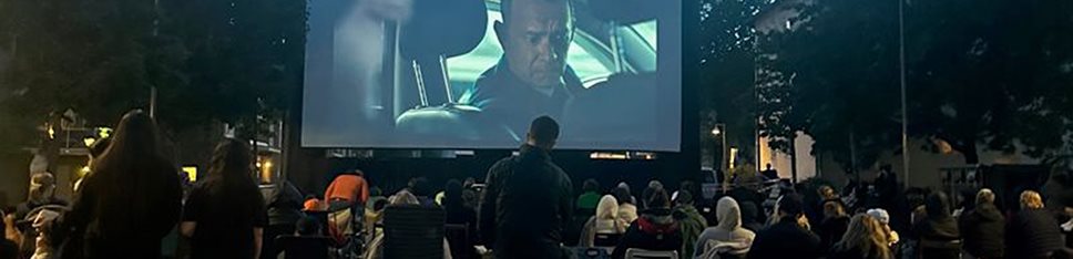 Människor framför stor utomhus-bioduk med Tom Hanks