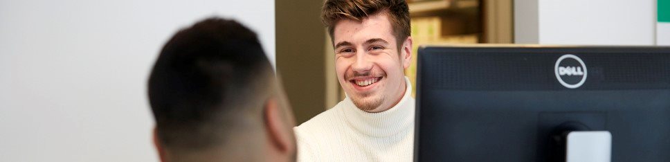 En man vid en datorskärm ler mot en man med bakhuvudet mot kameran