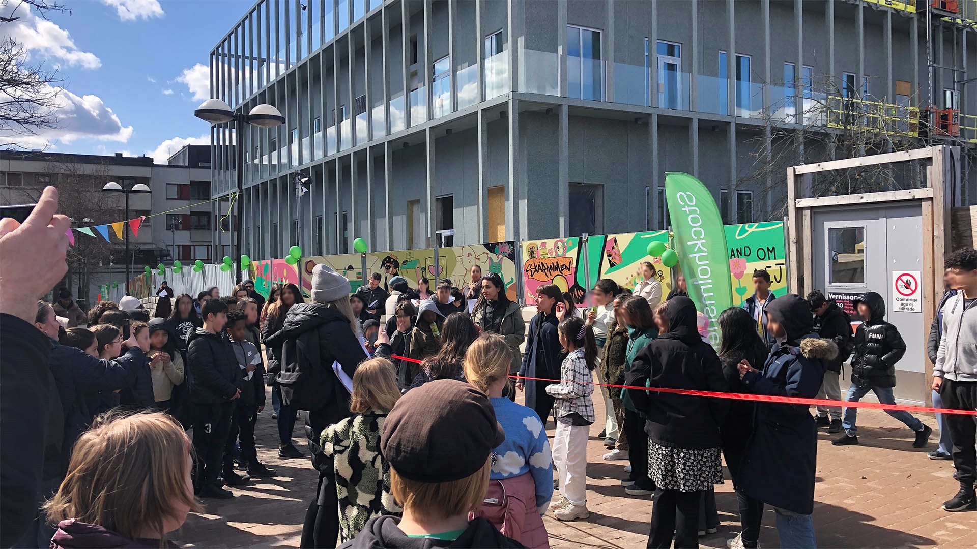Folksamling med barn och ungdomar intill byggarbetsplats