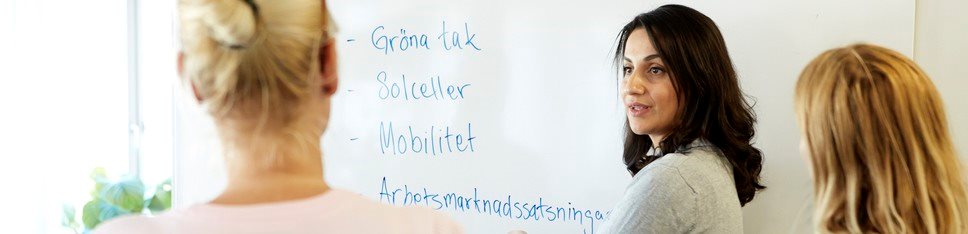 Tre kvinnor framför en whiteboard med orden "Gröna tak", "solceller" och "mobilitet".